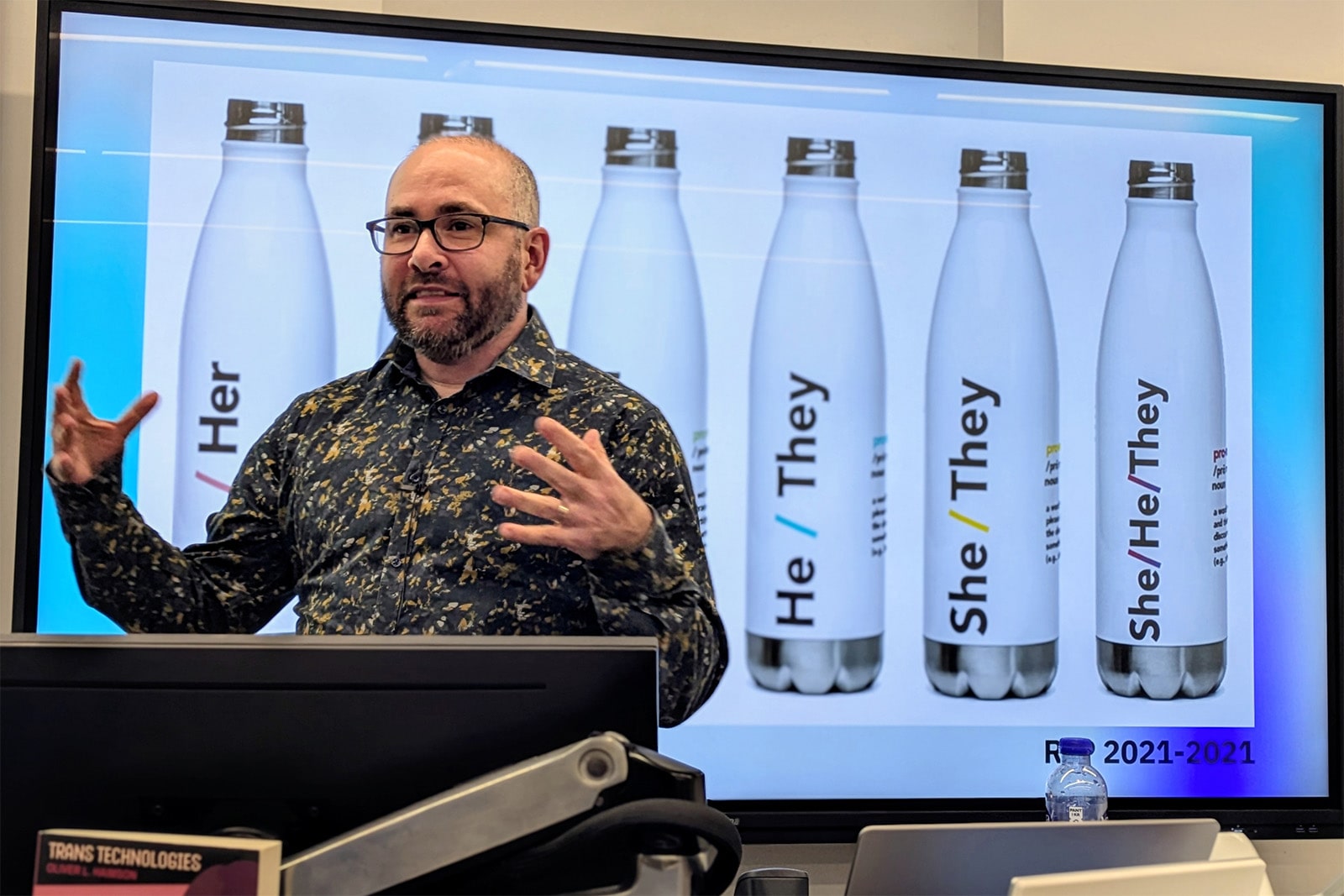 Oliver Haimson presents in front of a screen displaying a row of reusable bottles, each featuring a different set of pronouns.