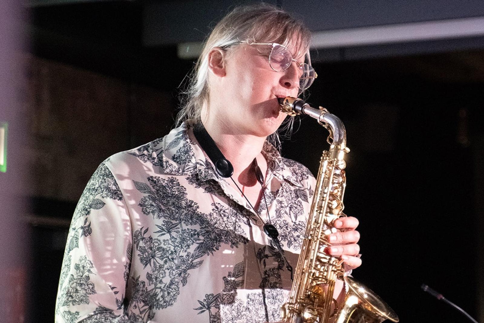 Person playing saxophone inside in a darkened room